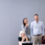 Ein verzweifelter Mann am Arbeitsplatz, während Kollegen über ihn lachen – Mobbing kann ernste Folgen haben. Ein Anwalt für Arbeitsrecht hilft, sich zu wehren.