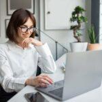 Lächelnde europäische Geschäftsfrau, die einen Laptop benutzt, online kommuniziert, E-Mails schreibt oder Kunden im Büro berät